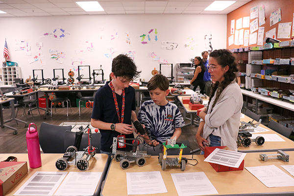 Two students work to fix robots while their teacher looks on