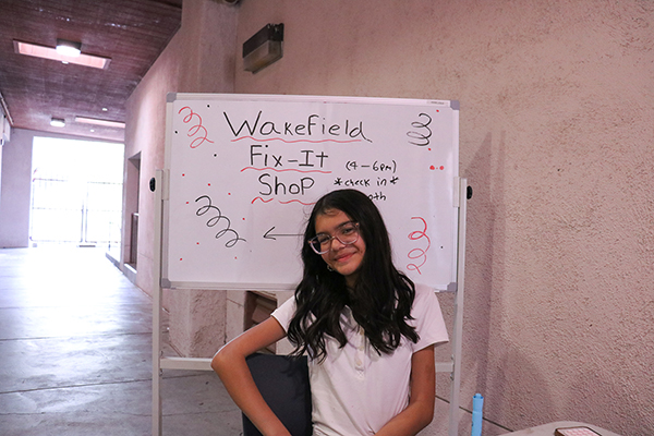 A girl smiles in front of the Wakefield Fix-It Shop sign on a whiteboard