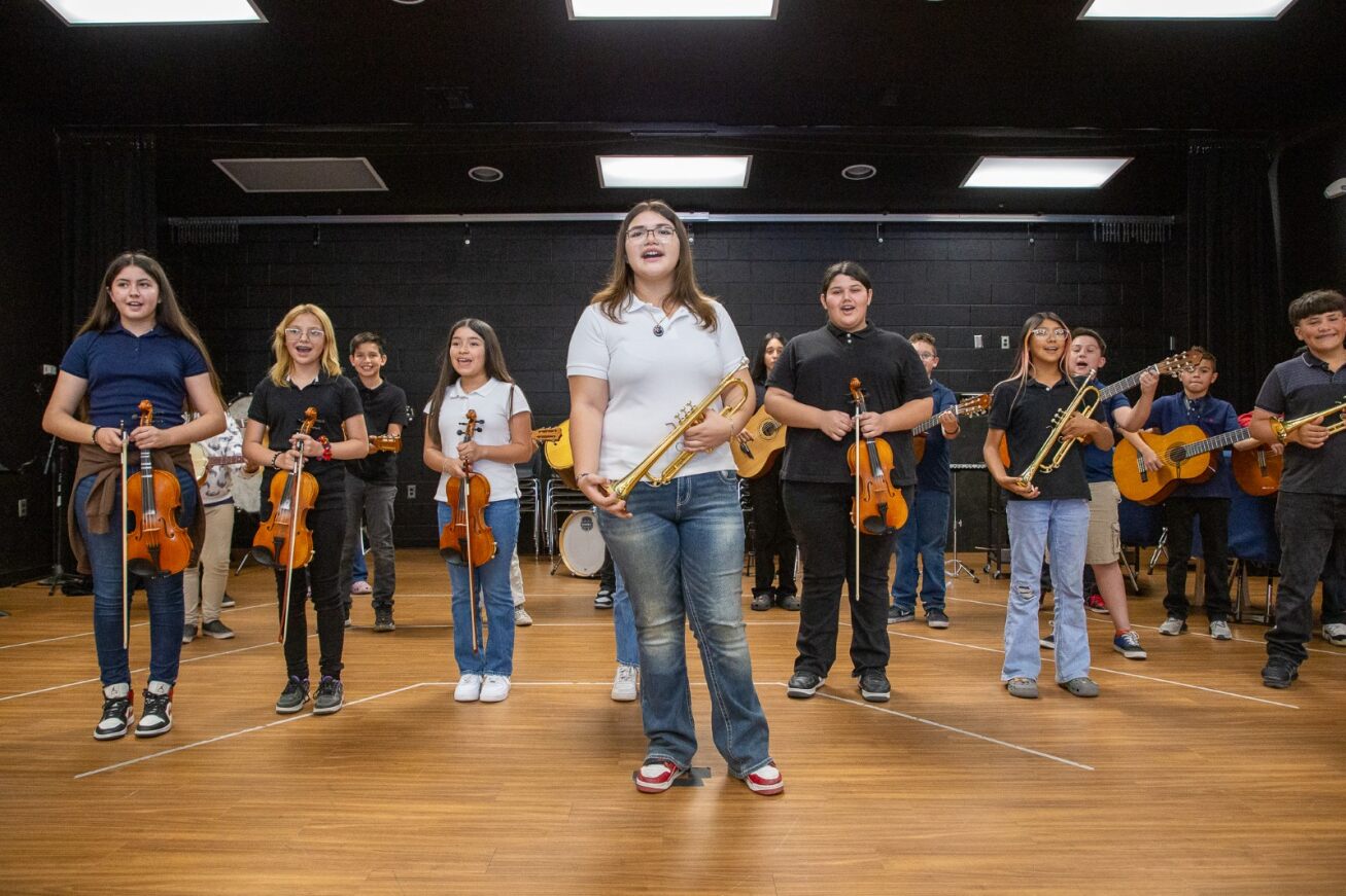 The mariachi class smiles and stands with their instruments